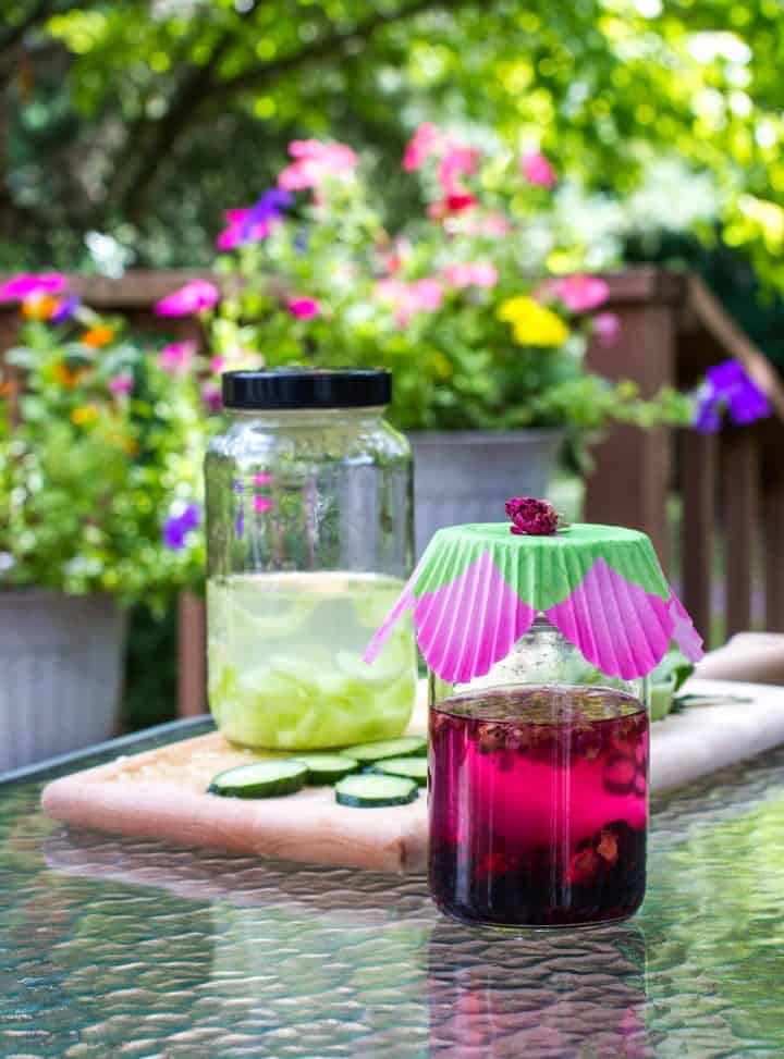 Two jars of vodka on table outdoors with cucumber and dried flowers for flavor