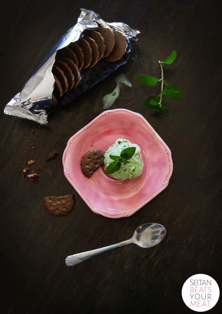 Thin mint ice cream on pink plate with spoon, mint leaves, and sleeve of Thin Mints on side