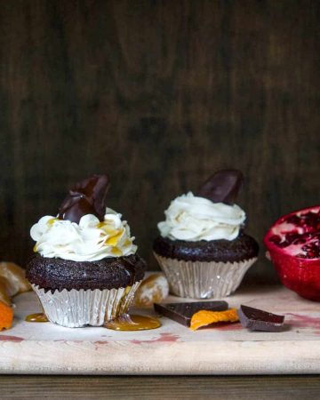 Chocolate cupcakes with white frosting on cutting board on dark background with pomegranate