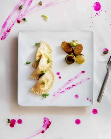 Potato pierogi, vegan kielbasa, and Brussels sprouts on white plate on white and pink background
