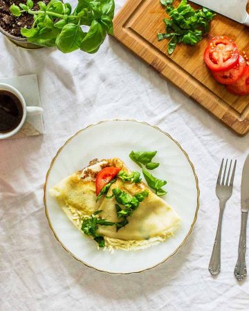 Crepe with tomato and basil on white and gold plate on white tablecloth