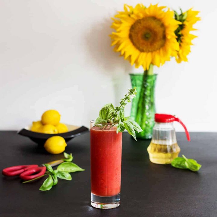 Glass of watermelon fresca with basil with vase of sunflowers, lemons, and decorative items in background
