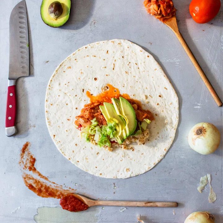 Overhead photo of large tortilla with tinga and avocado on top surrounded by vegetables