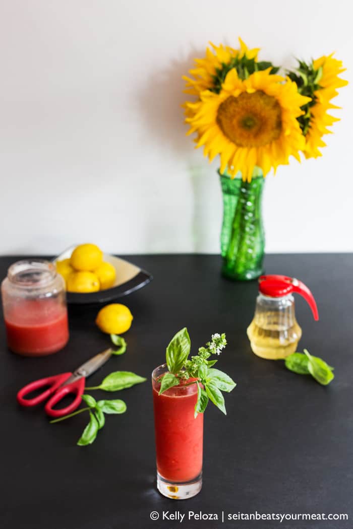 Watermelon agua fresca in glass with fresh basil garnish with flowers and lemons in background