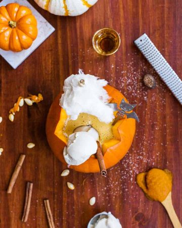 Pumpkin milkshake in carved out pie pumpkin surrounded by pumpkin seeds and baking supplies