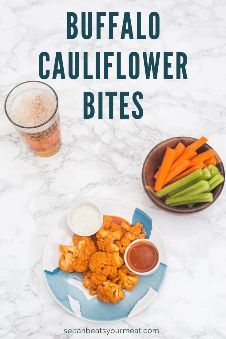 Plate of buffalo cauliflower on marble background with bowl of carrot and celery sticks and beer in pint glass