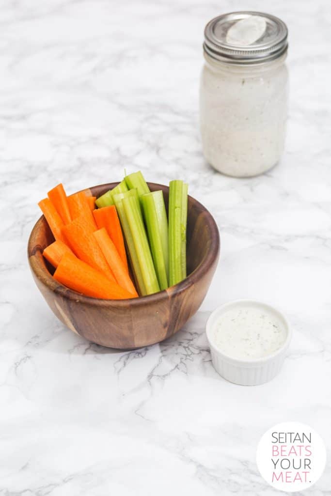 Small cup of ranch dressing with carrot and celery sticks in bowl