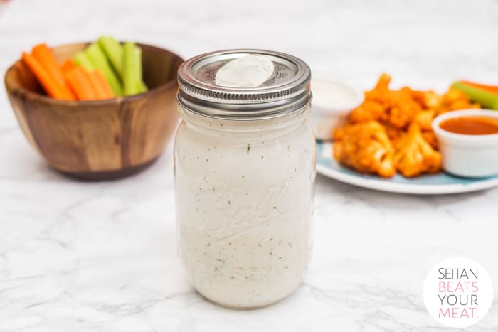 Mason jar of ranch dressing with plates of food in background
