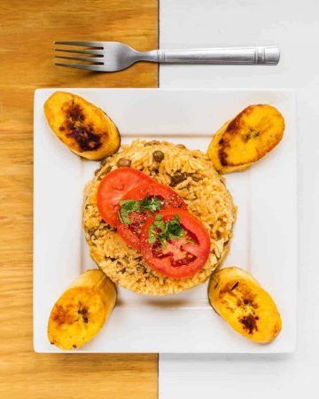 Plate of arroz con gandules with plantains on white and wooden surface