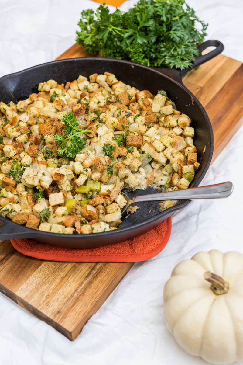Spoon in a cast iron pan filled with stuffing on top of a cutting board with a bunch of parsley in the background
