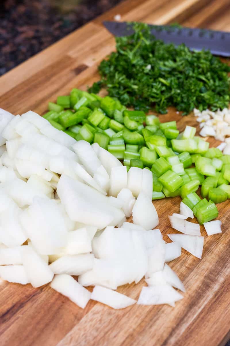 Chopped onions, celery, and parsley on wooden cutting board