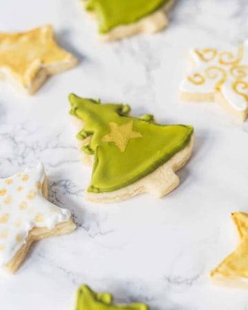 Decorated Christmas tree and star-shaped sugar cookies on marble surface