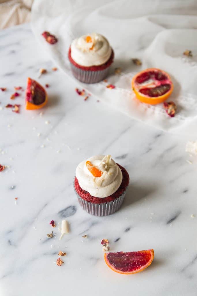 Red velvet cupcakes with frosting on marble background with blood orange slices