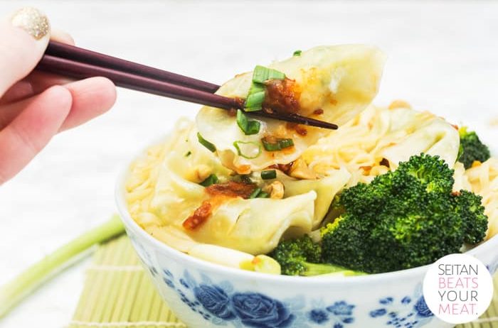 Gyoza being lifted out of bowl of noodles with hand holding chopsticks