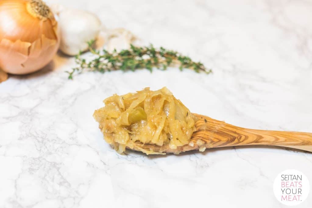 Wooden spoon with caramelized onions on marble counter with thyme and onion in background