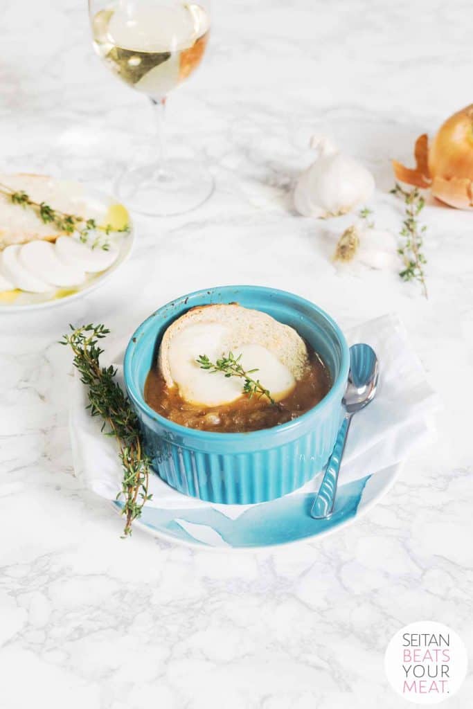 Bowl of vegan French onion soup on marble surface with glass of white wine