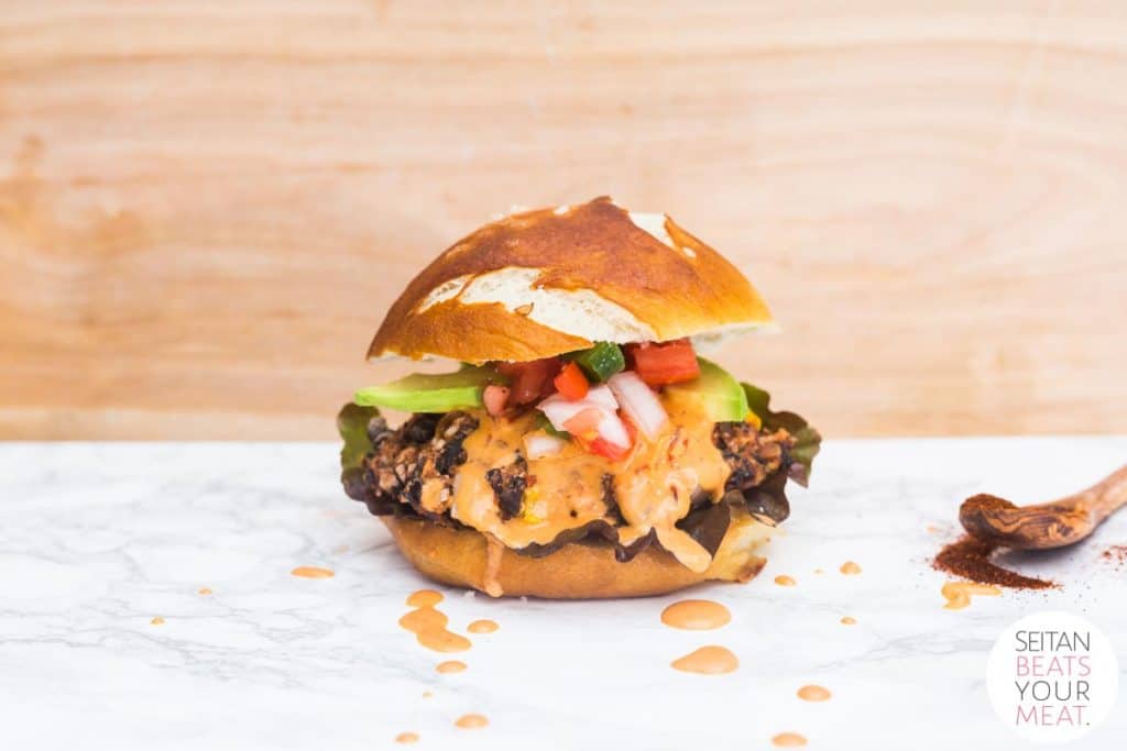Black bean burger with chipotle sauce dripping down sides on marble counter with wooden background