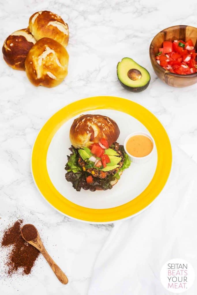 Black bean burger on pretzel bun on yellow plate on white marble counter