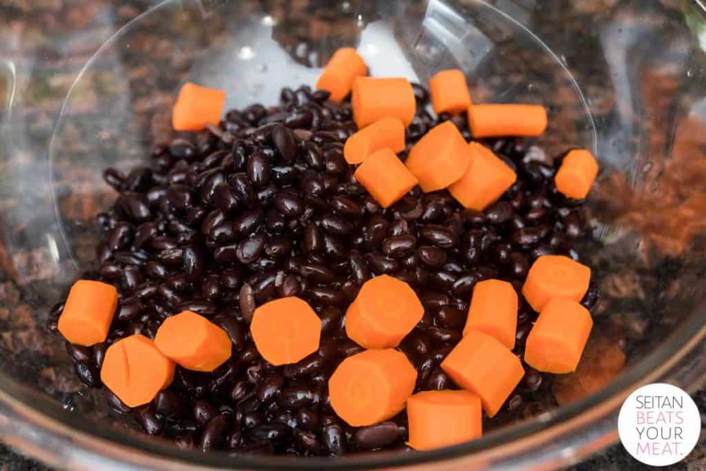 Big glass bowl filled with black beans and chopped cooked carrots