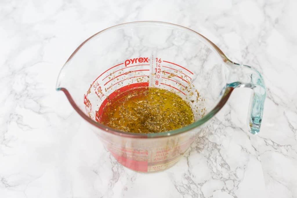 Glass measuring cup on white marble surface filled with marinade