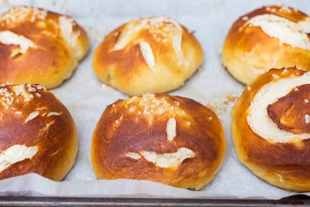 Six baked pretzel buns on baking tray with parchment paper