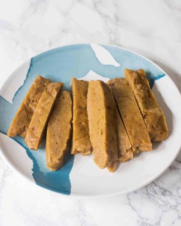 Plate of sliced seitan on plate on white marble background