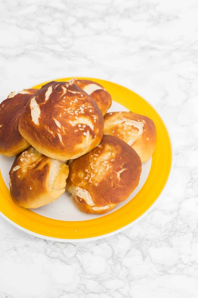 Pretzel buns with coarse salt on yellow plate on white marble surface