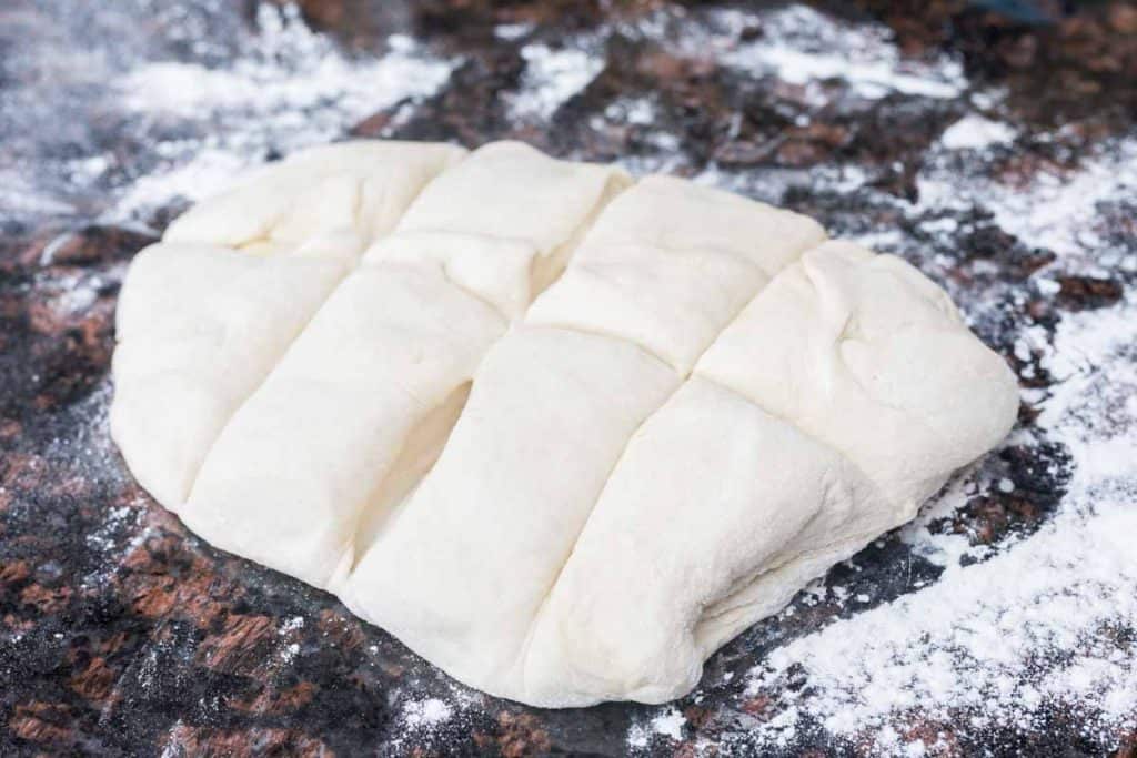 Slab of dough divided into eight pieces on granite counter