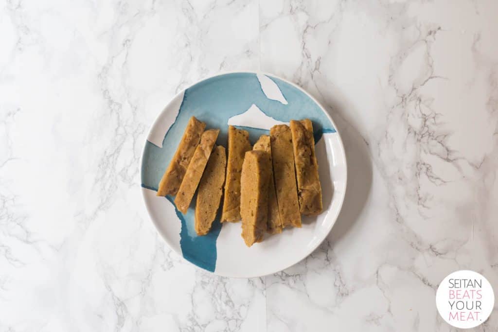 Plate of sliced seitan on plate on white marble background