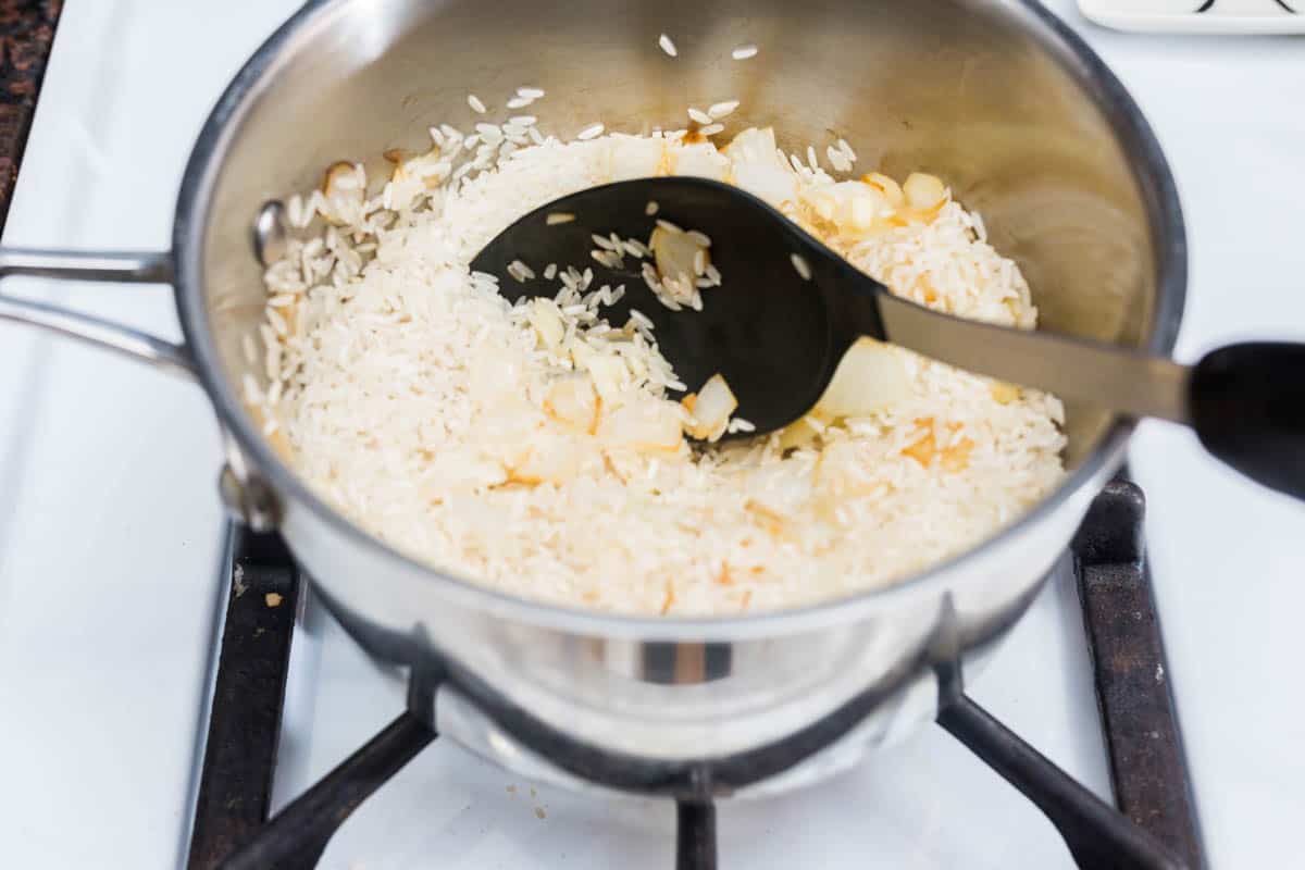 Pot of rice and onions on stove with plastic spoon