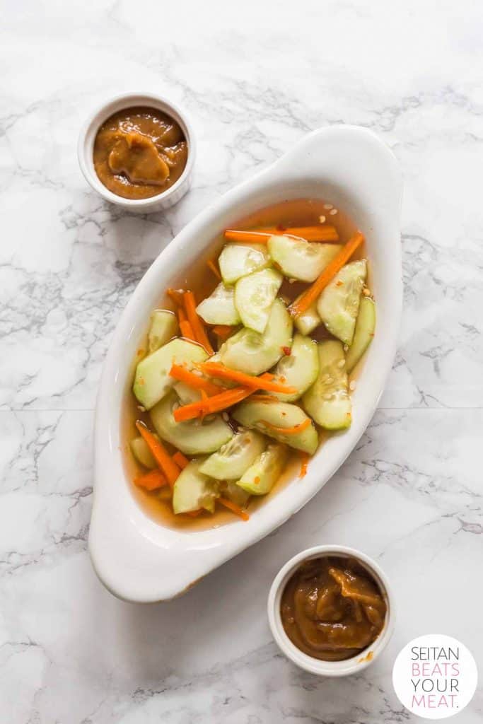 Bowl of cucumber salad with side of peanut sauce on white marble counter