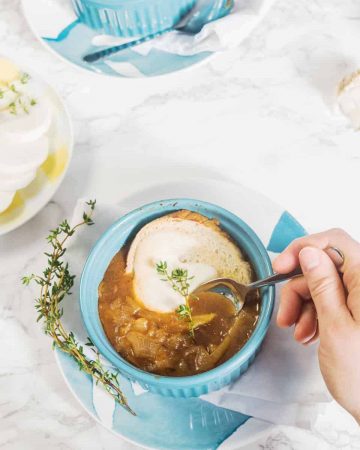 Vegan French onion soup in blue bowl on marble surface