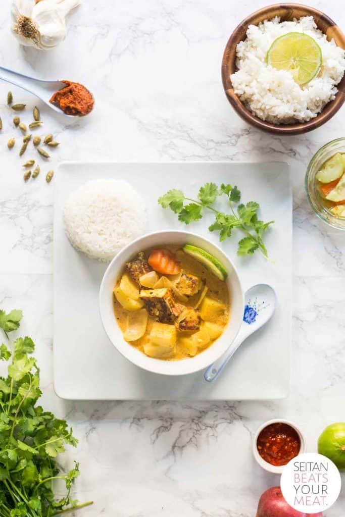 Bowl of yellow curry in bowl on plate with rice surrounded by curry ingredients
