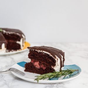 Slice of chocolate cake on plate with sprig of rosemary