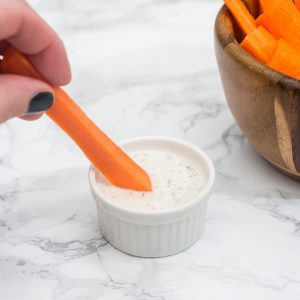 Hand dipping carrot stick in ranch dressing