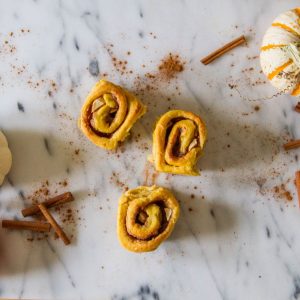 Pumpkin cinnamon rolls on marble counter surrounded by cinnamon sticks
