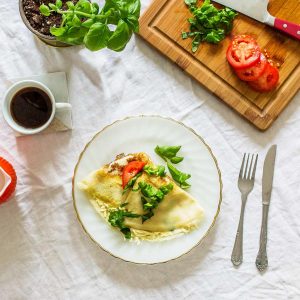 Crepe with tomatoes and basil on white plate on white tablecloth with table settings