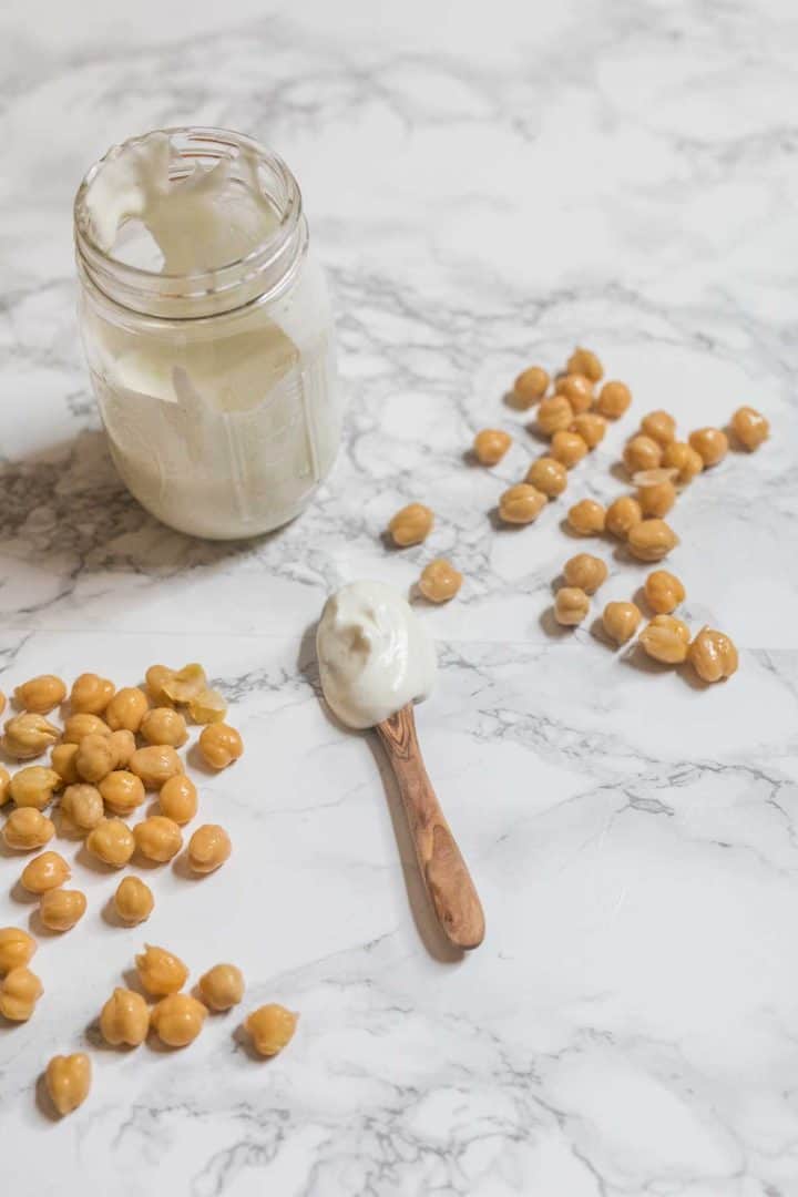 Spoonful of mayonnaise on table with chickpeas scattered