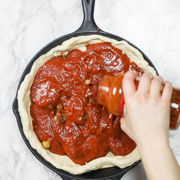 Hand pouring tomato sauce on pizza dough in cast iron pan
