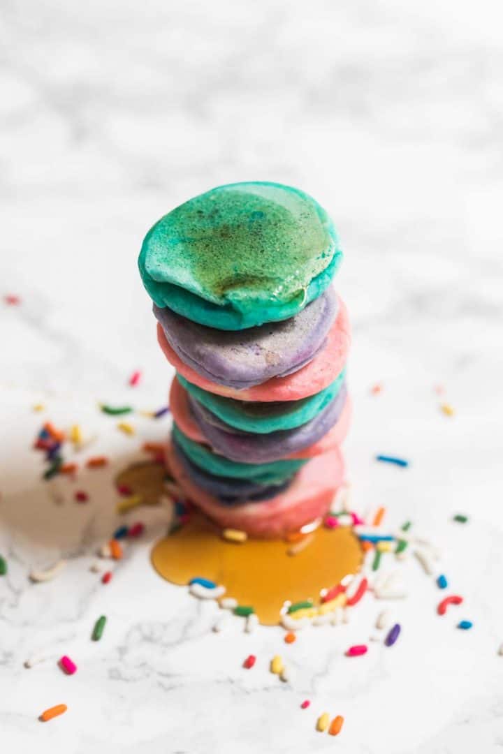 Tall stack of tiny colorful pancakes with syrup and rainbow sprinkles