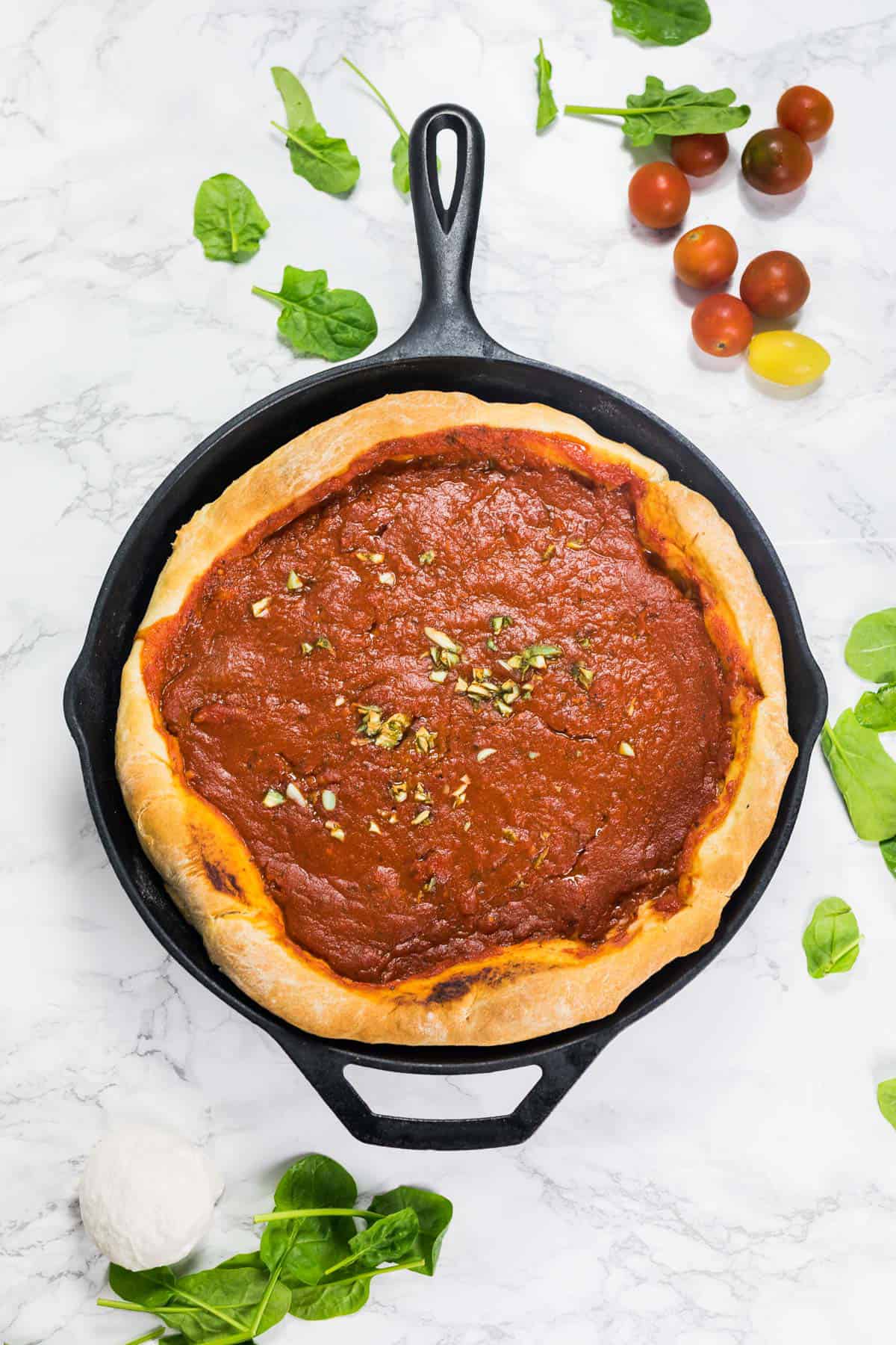 Deep dish pizza baked in a cast iron pan on marble counter