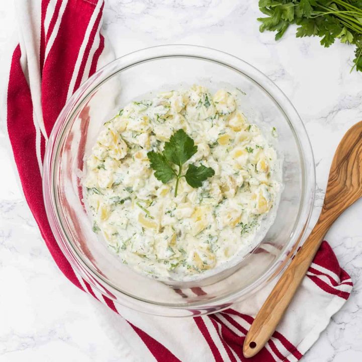 Large bowl of potato salad with wooden spoon and dish towel