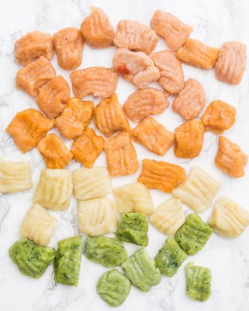 Red, orange, plain, and green gnocchi on marble counter