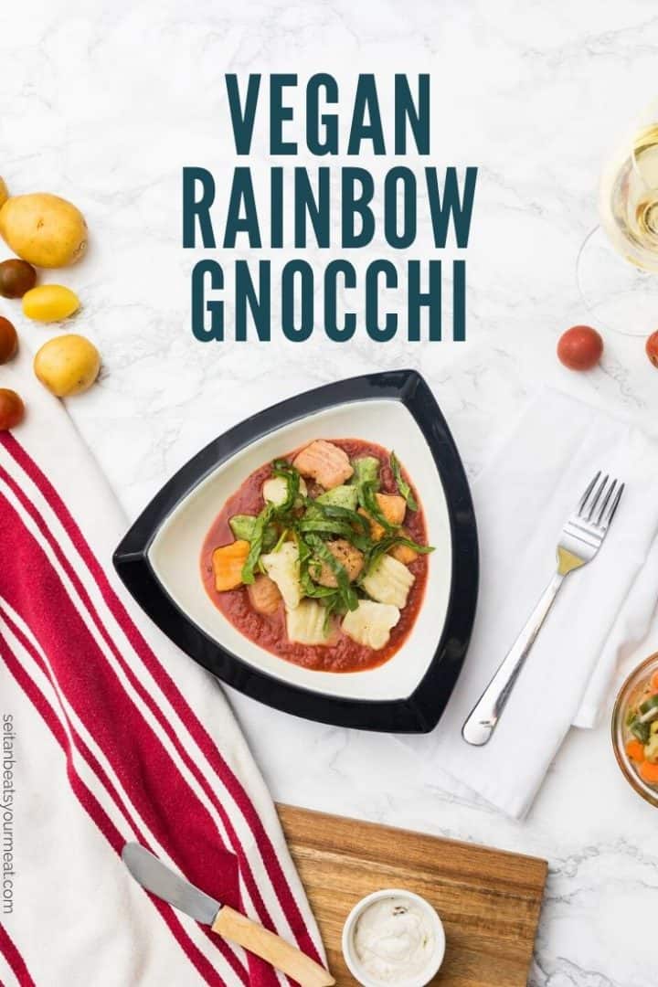 Bowl of gnocchi with tomato sauce in table setting with text "Vegan Rainbow Gnocchi"