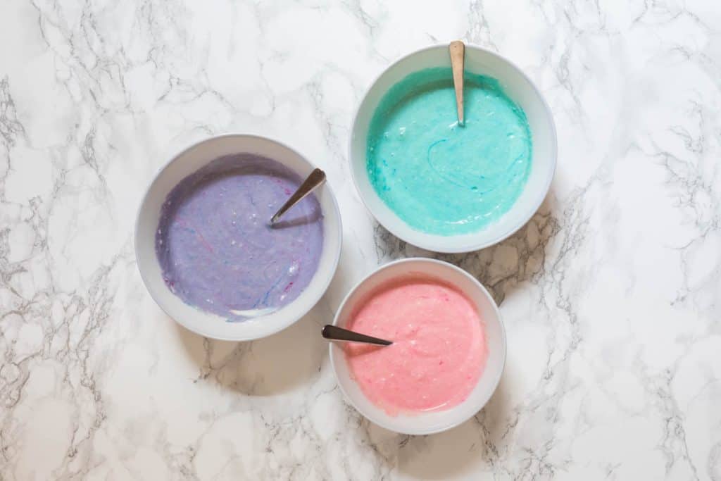 Three bowls of pancake batter dyed blue, pink, and purple