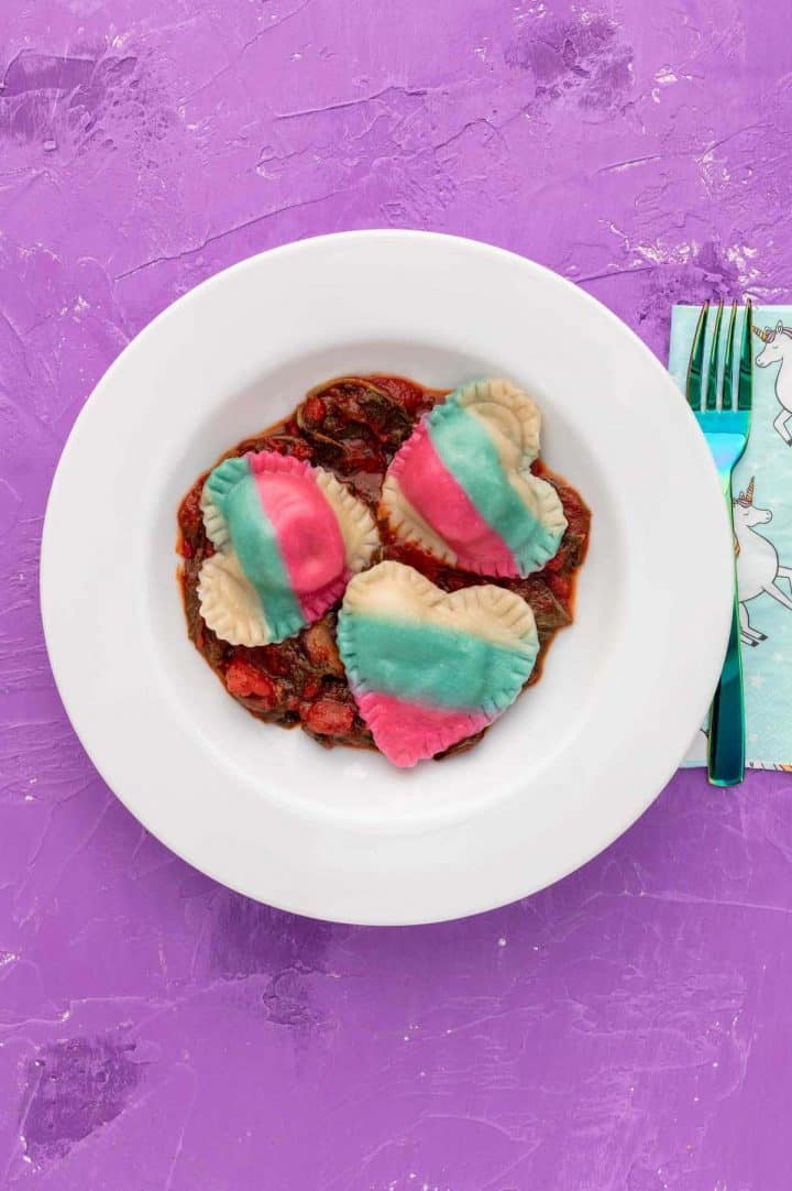 Pink, blue, and white heart-shaped ravioli in a bowl with marinara sauce