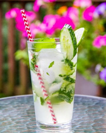Cucumber mojito with mint, limes, and cucumbers in a pint glass with a red straw