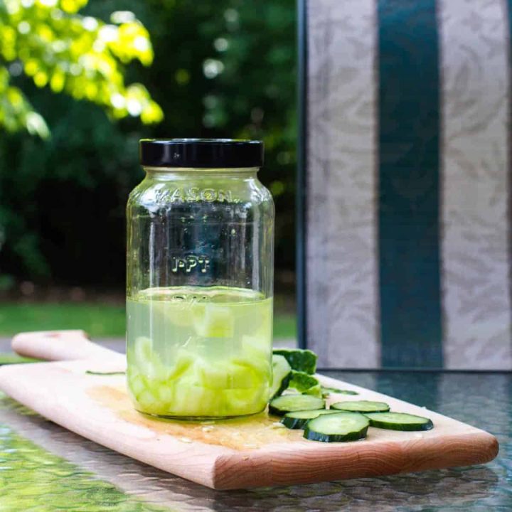 Jar of cucumber vodka on cutting board outdoors with cucumber slices