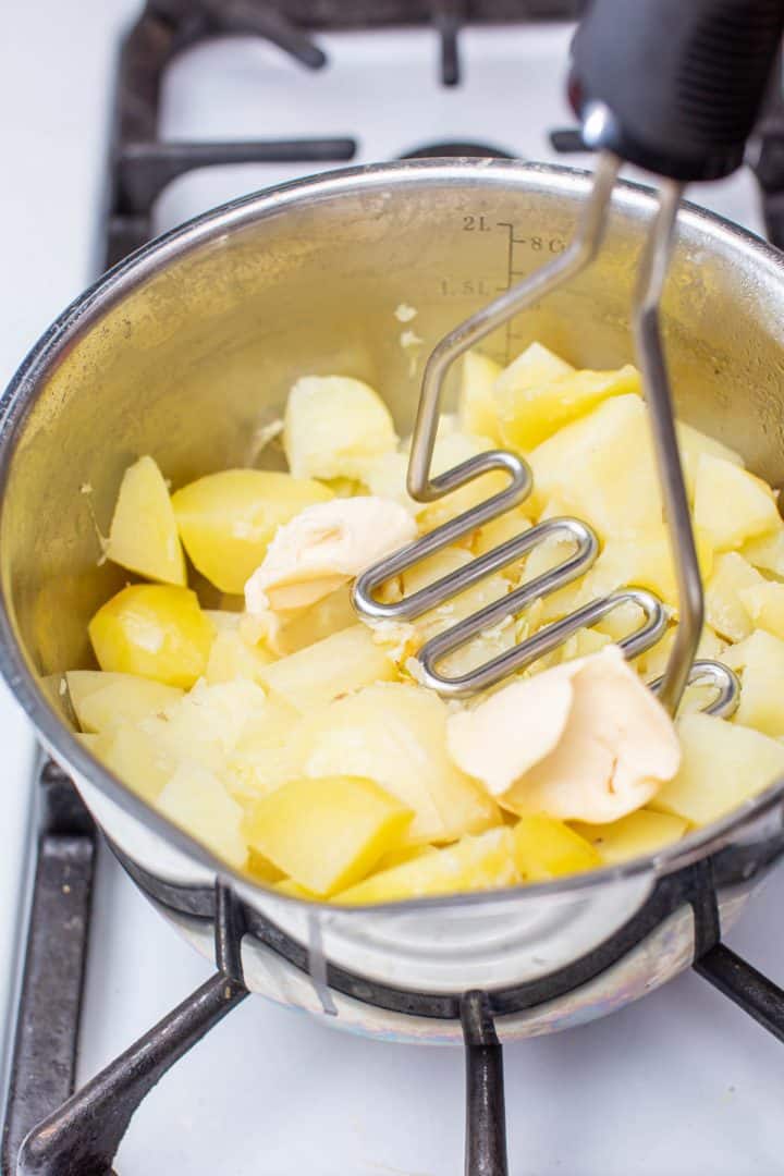 Cooked potatoes in pot with butter and potato masher