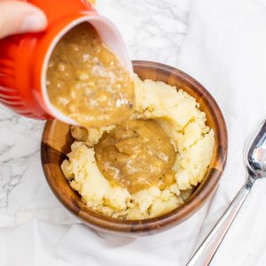 Hand pouring gravy into bowl of mashed potatoes